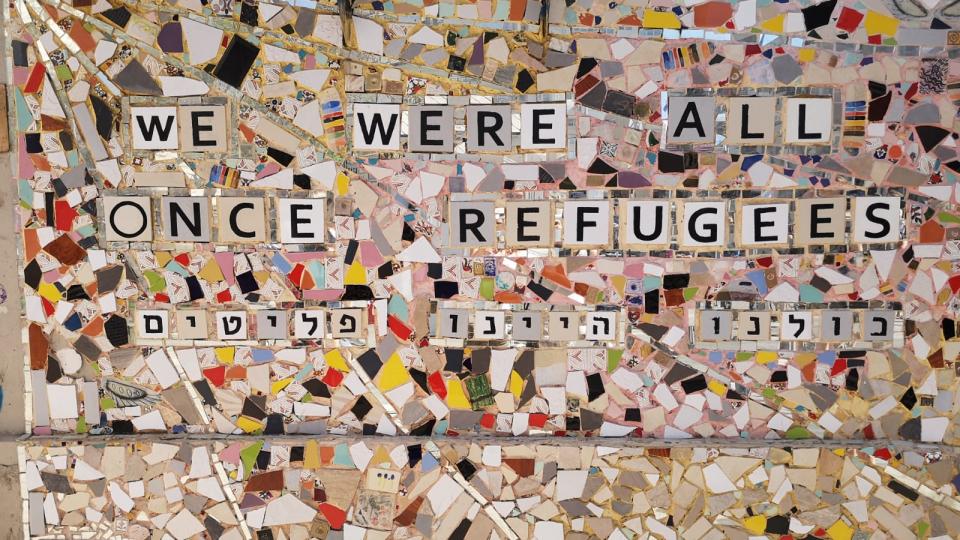 Ein Gemälde aus weißem und buntem Mosaikglas, auf dem "we were all once refugees" (zu Deutsch: Wir waren alle einmal Flüchtlinge) steht.