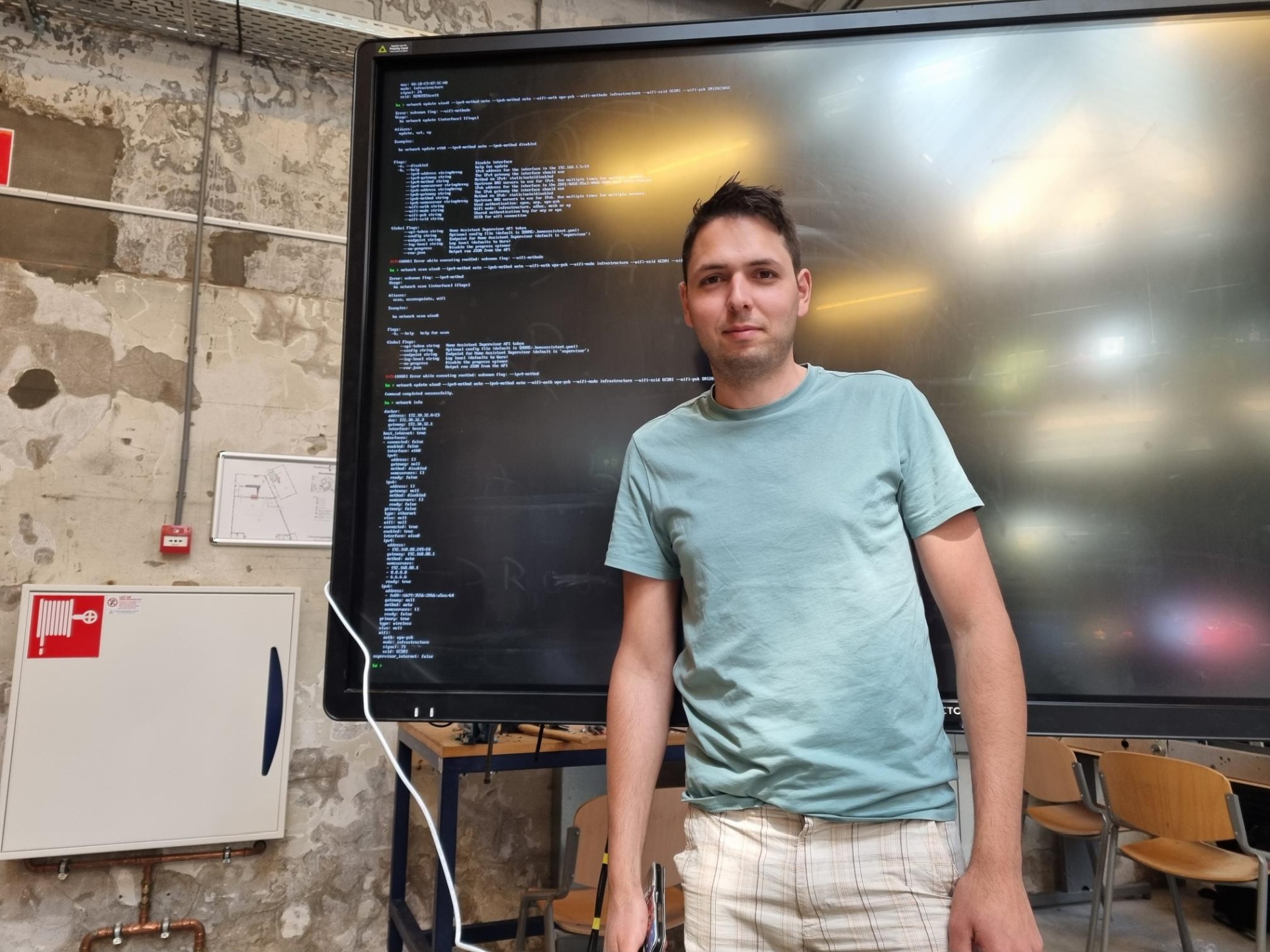Ein junger Mann steht vor einem großen Bildschirm auf dem die Ausgabe eines Computers angezeigt wird.