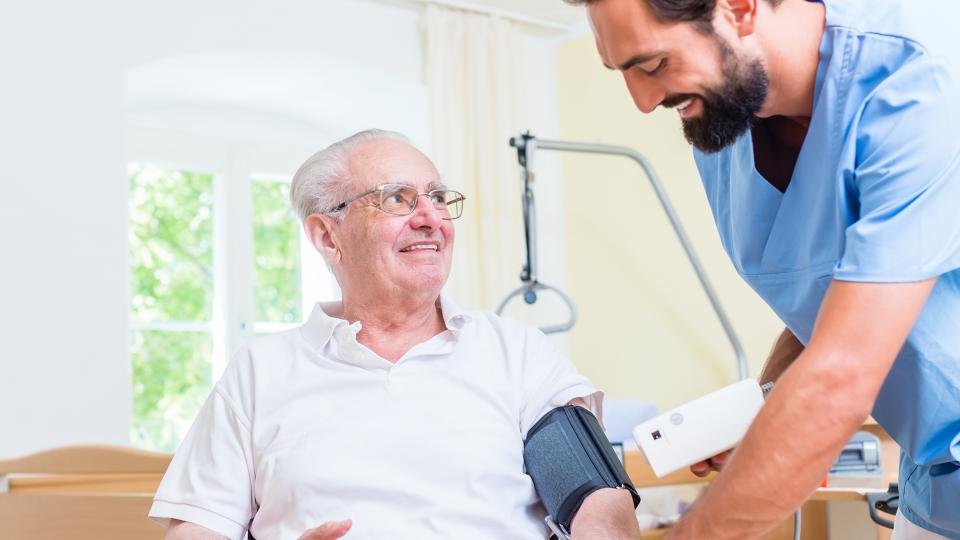 Ein medizinischer Fachangestellter misst in einem Krankenhaus den Blutdruck eines älteren Mannes. 