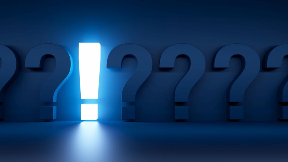 Vor einer dunkelblauen Wand stehen sechs Fragezeichen, die sich farblich kaum vom Hintergrund abheben. Etwas links von der Mitte steht ein hell erleuchtetes Ausrufezeichen. 
