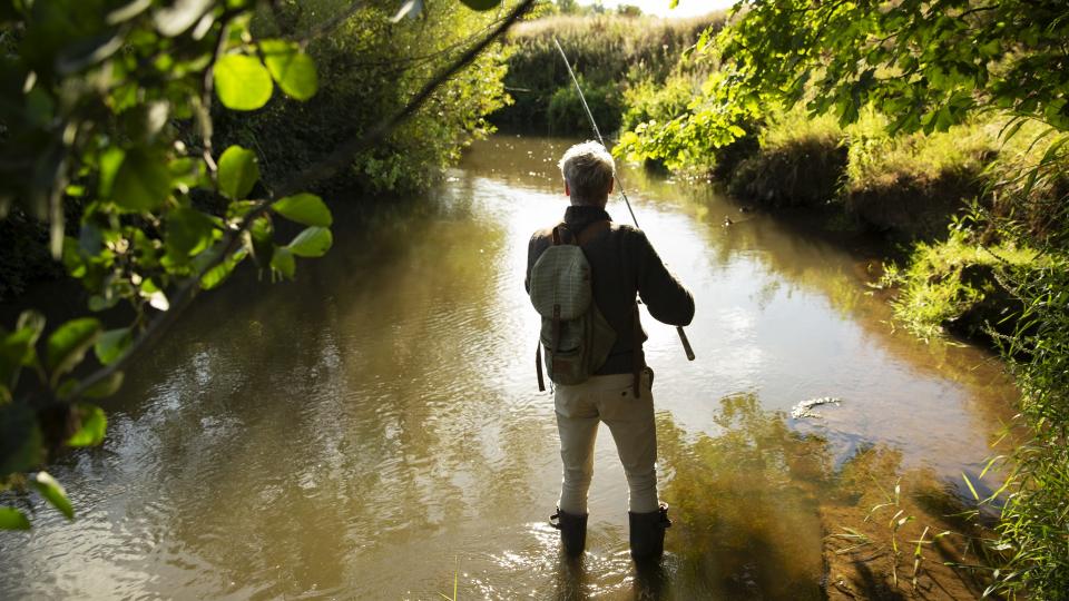 Ein Angler, der sich in der Natur befindet und in seichtem Gewässer angelt. 