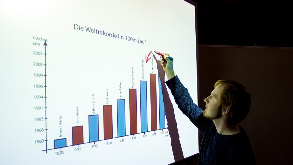 Ein Mann analysiert die Weltrekorde im 100-Meter-Lauf von 1960 bis 2007 anhand eines Balkendiagramms.