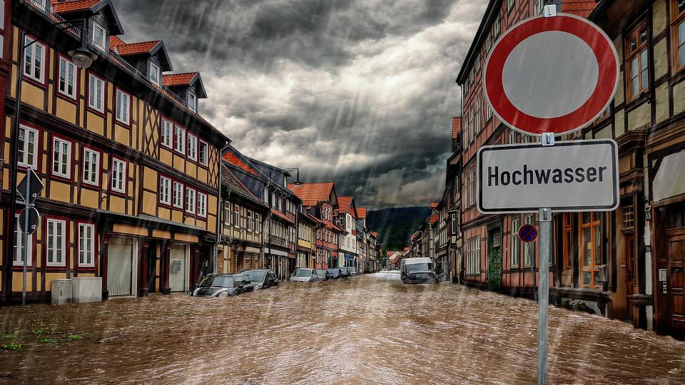 Bild einer überfluteten Straße, davor ein Schild "Durchfahrt verboten - Hochwasser"