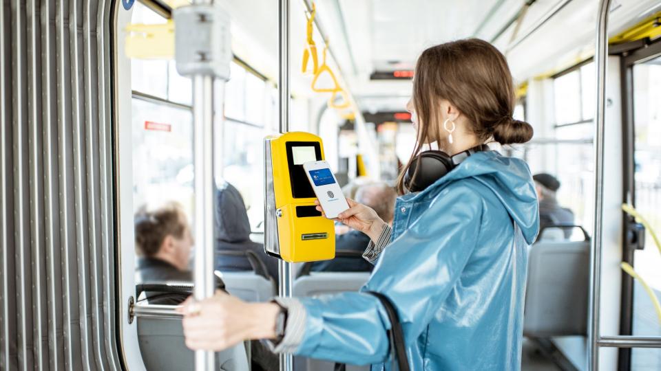 Eine Frau bezahlt kontaktlos mit ihrem Smartphone in einer Straßenbahn.