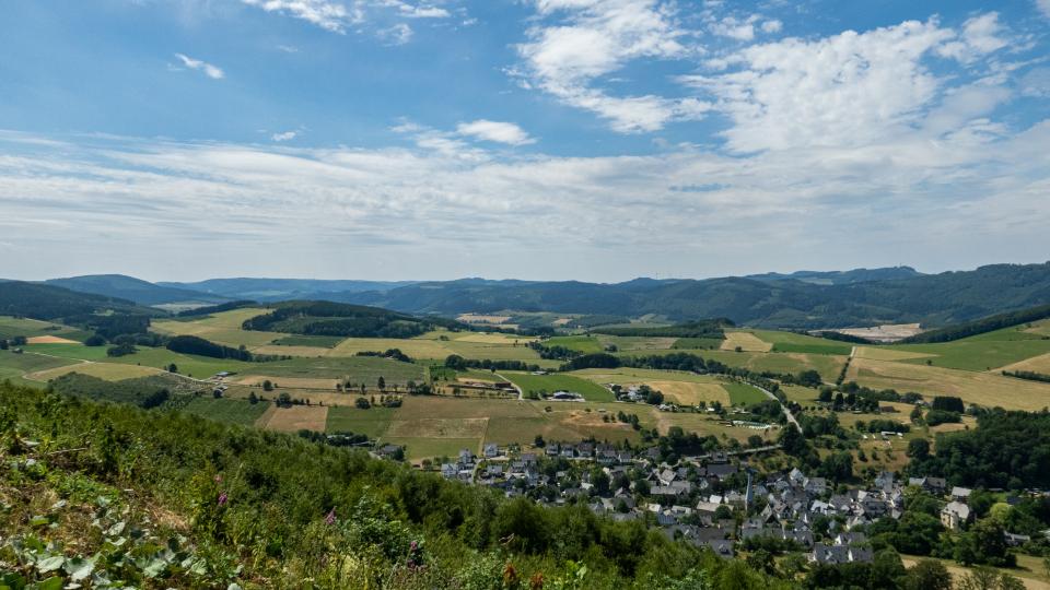 Blick auf ein Dorf in einem Tal inmitten von Feldern.