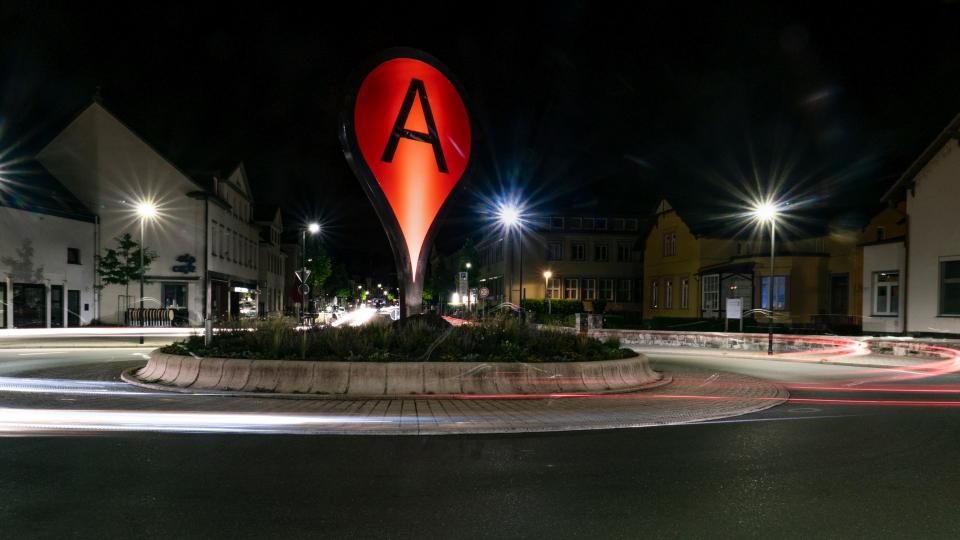 Bild eines Kreisverkehrs mit einem roten Google-Pin "A" in der Mitte bei Nacht.