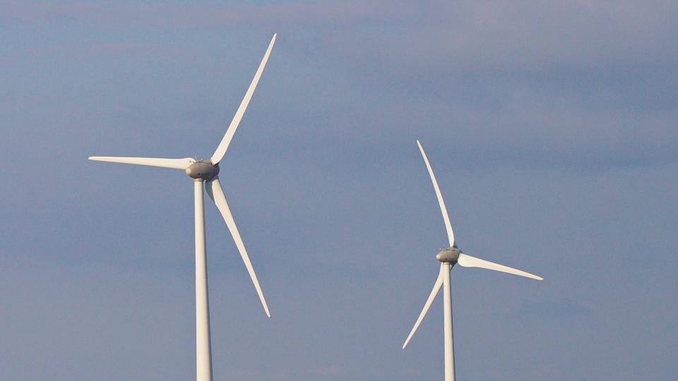 Zwei Windräder vor bewölktem, aber blauem Himmel.