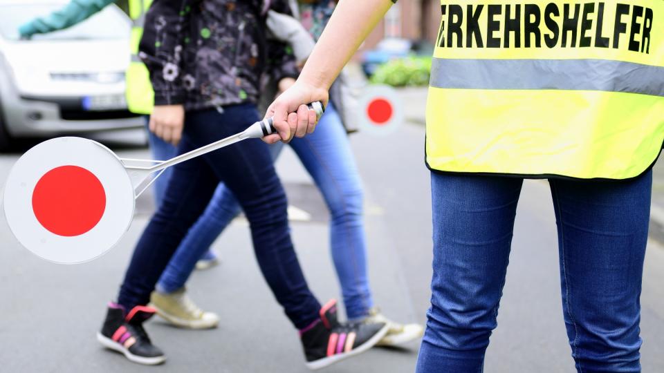 Bild eines Verkehrshelfers, der Schülern das Überqueren einer Straße ermöglicht.