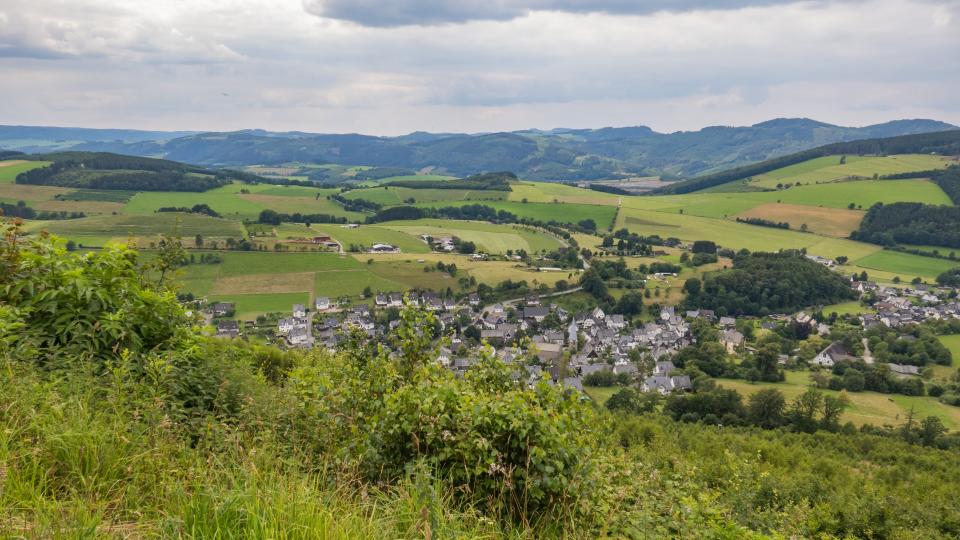 Blick von einem Hügel auf ein im Tal gelegenes Dorf.