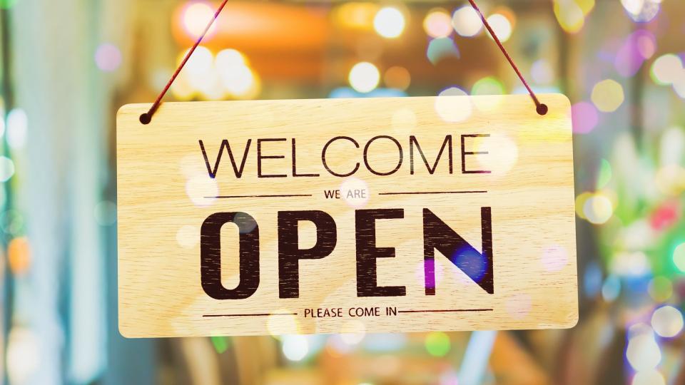 Ein Schild, "Welcome we are open" an einer Glastür.