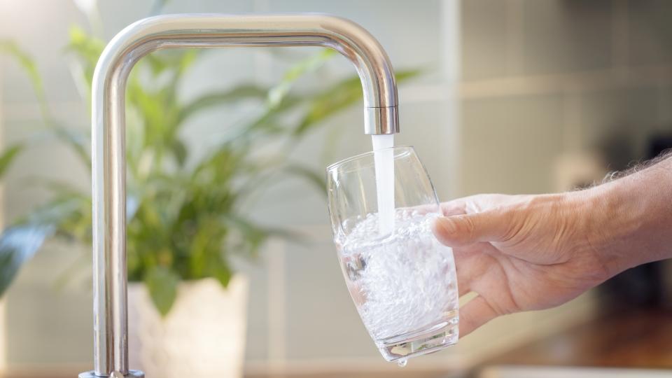 Ein Glas wird mit Wasser aus einem Wasserhahn befüllt