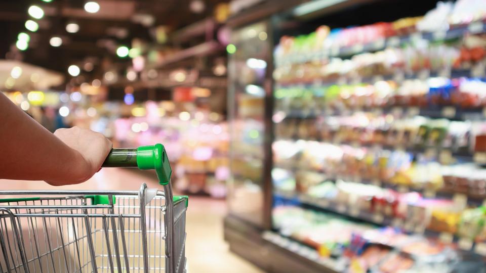 Eine Person schiebt einen Einkaufswagen durch einen Supermarkt. 