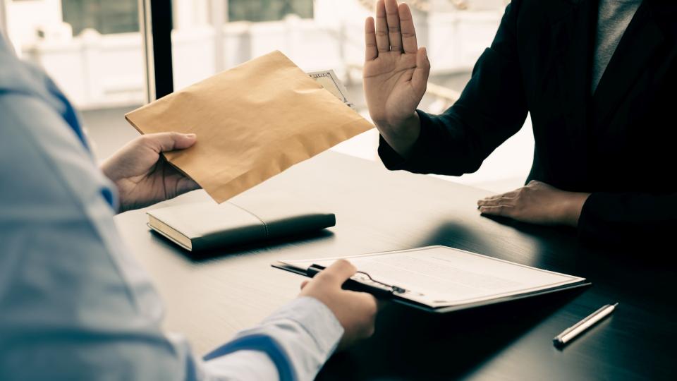 Eine Person bietet einer ablehnenden Person einen Umschlag an