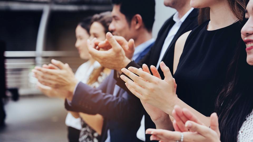 Schick gekleidete Frauen und Männer stehen in einer Reihe und applaudieren.