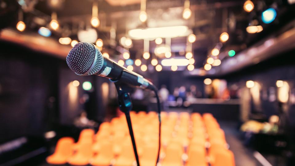 Abgebildet ist ein Mikrofon vor einem leeren Theatersaal.