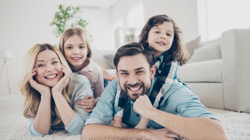 Eine Familie liegt lachend auf dem Boden in einer gemütlichen Wohnung