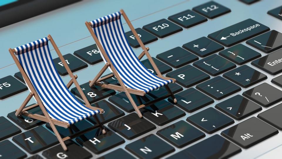 Zwei gestreifte Sonnenstühle stehen in Miniaturform auf einer beleuchteten grauen Tastatur von einem Laptop