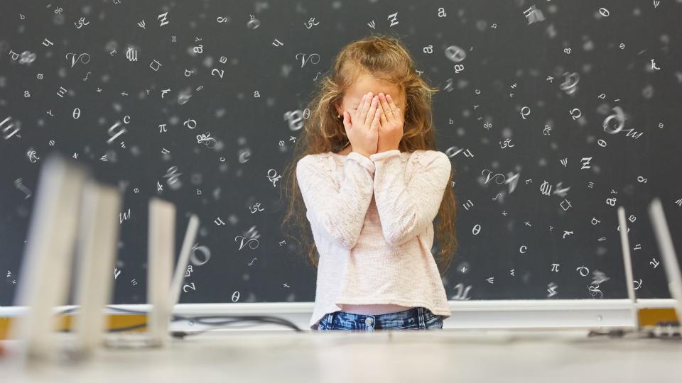 Kind in Schule vor Tafel mit fliegenden Buchstaben verdeckt sich die Augen