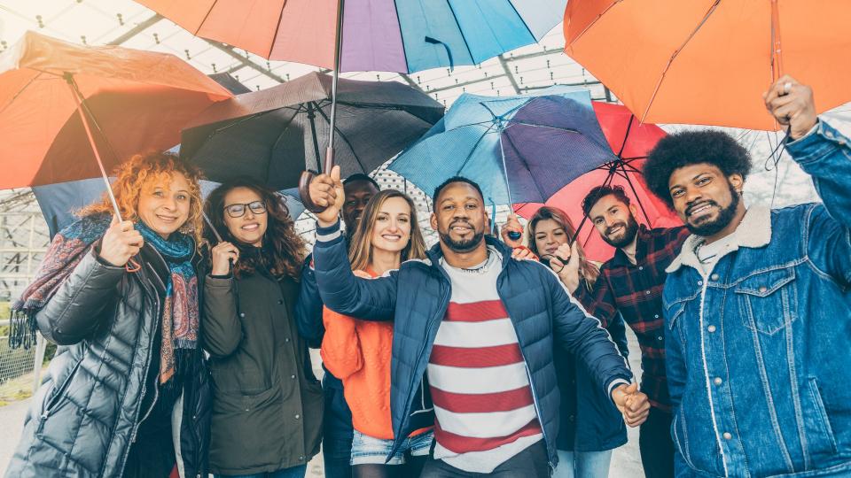 Eine Gruppe mit freundlich schauenden Personen verschiedener Nationen mit Regenschirmen in den Händen