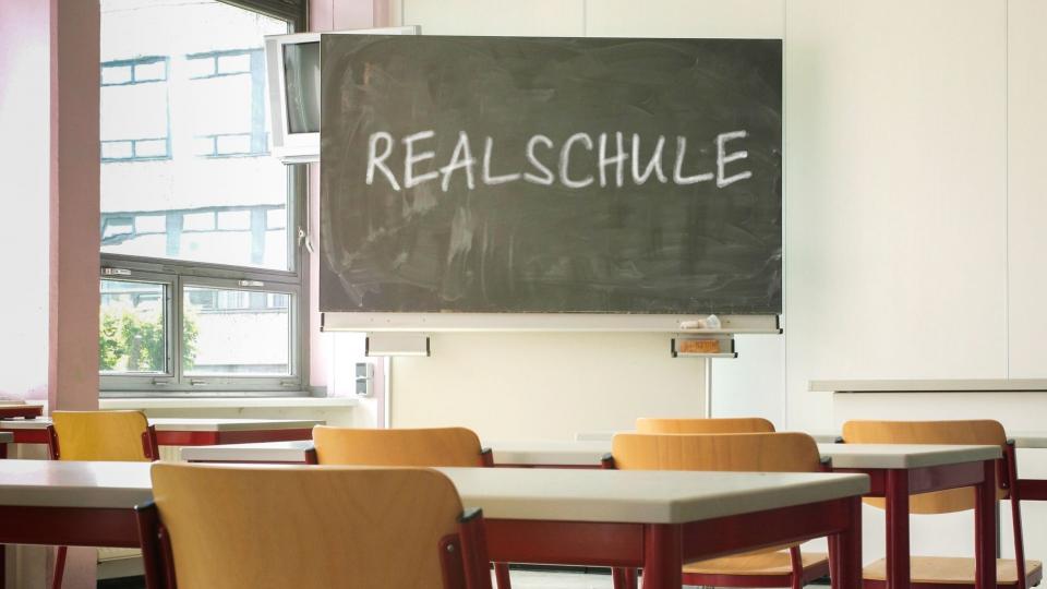 Ein Klassenraum mit einer Tafel auf der das Wort Realschule steht.