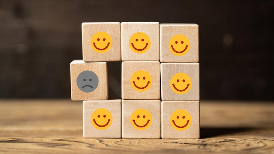 Viele Würfel mit lächelnden Smileys und einer der unzufrieden ist