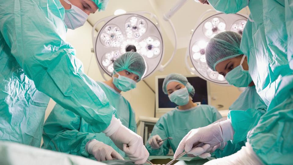 Ein Team aus Ärztinnen und Ärzten operiert eine Person in einem Operationssaal.