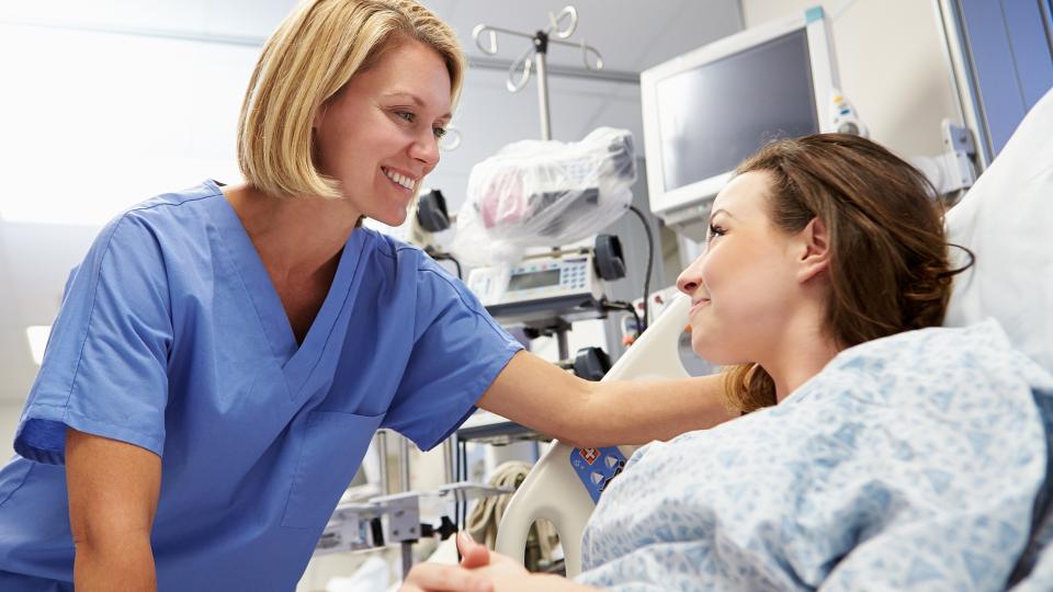 Eine Pflegefachfrau betreut eine Patientin, die in einem Krankenbett im Krankenhaus liegt.