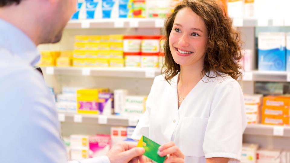 Eine Pharmazeutisch-Technische Assistentin nimmt in einer Apotheke die Gesundheitskarte eines Kunden entgegen.