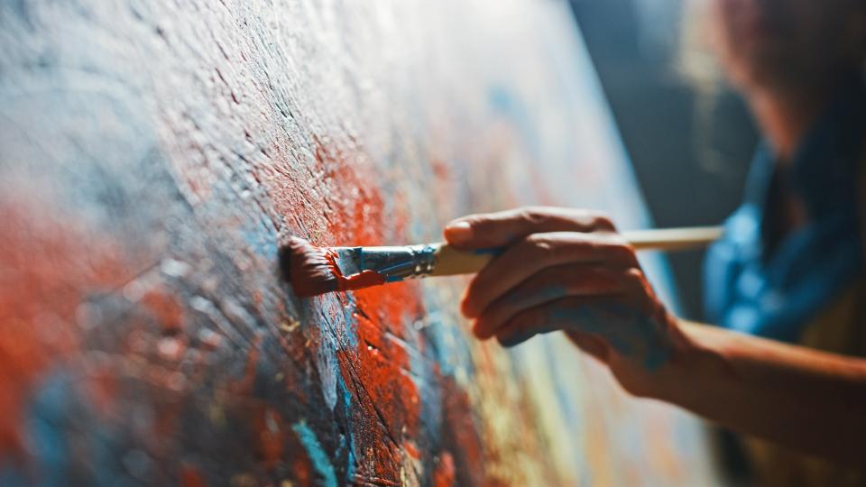 Nahaufnahme von einer Hand mit einem Pinsel wie dieser über eine Leinwand geführt wird