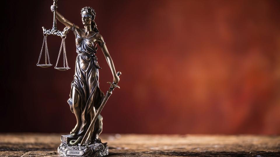 Abgebildet ist die Justitia als Bronzefigur. Sie ist das Symbol für Gerechtigkeit und Rechtspflege. In der rechten Hand trägt sie eine Pendelwaage und in der linken Hand ein Schwert. Ihre Augen sind mit einem Stück Stoff verbunden. 