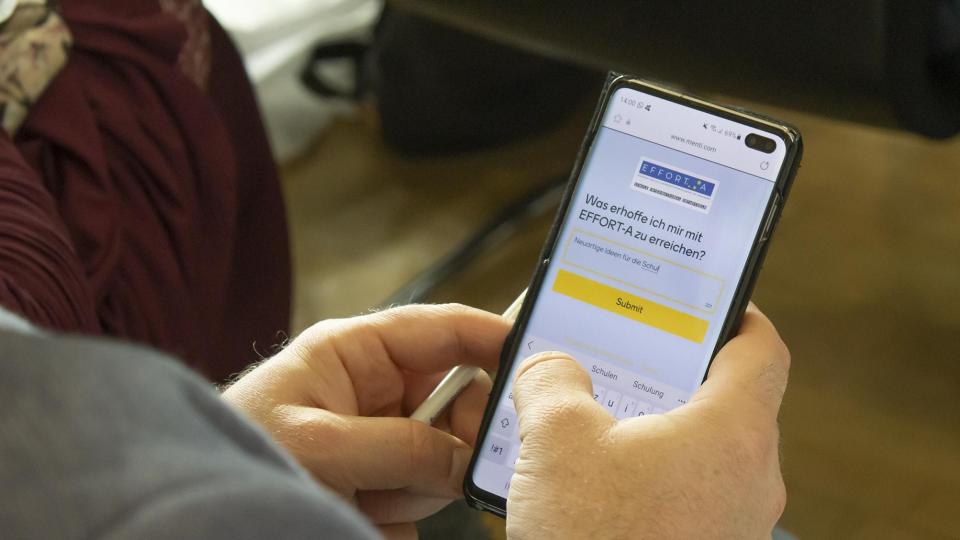 Eine Person hält ein Handy in den Händen. Auf dem Bildschirm ist die Frage "Was erhoffe ich mir mit EFFORT-A zu erreichen?" eingeblendet. 