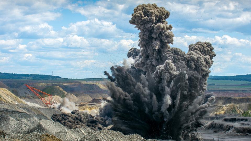 Abgebildet ist eine Explosion auf einem großen Gelände im Tagebau.
