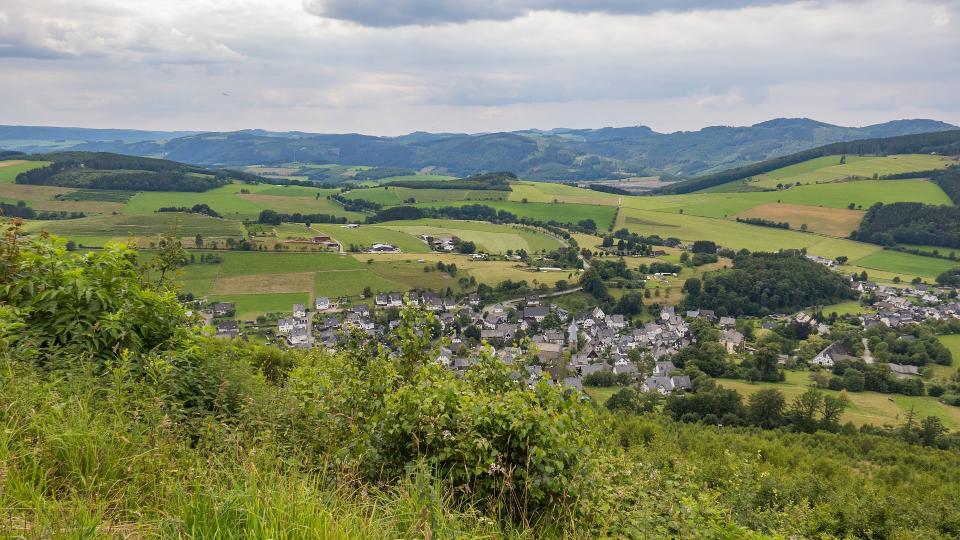 Abgebildet ist das Panorama eines Dorfs in ländlicher Umgebung.