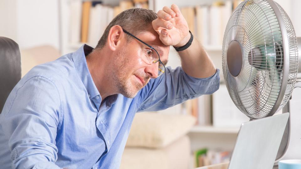 Ein Mann arbeitet schwitzend am Laptop vor einem laufenden Ventilator.