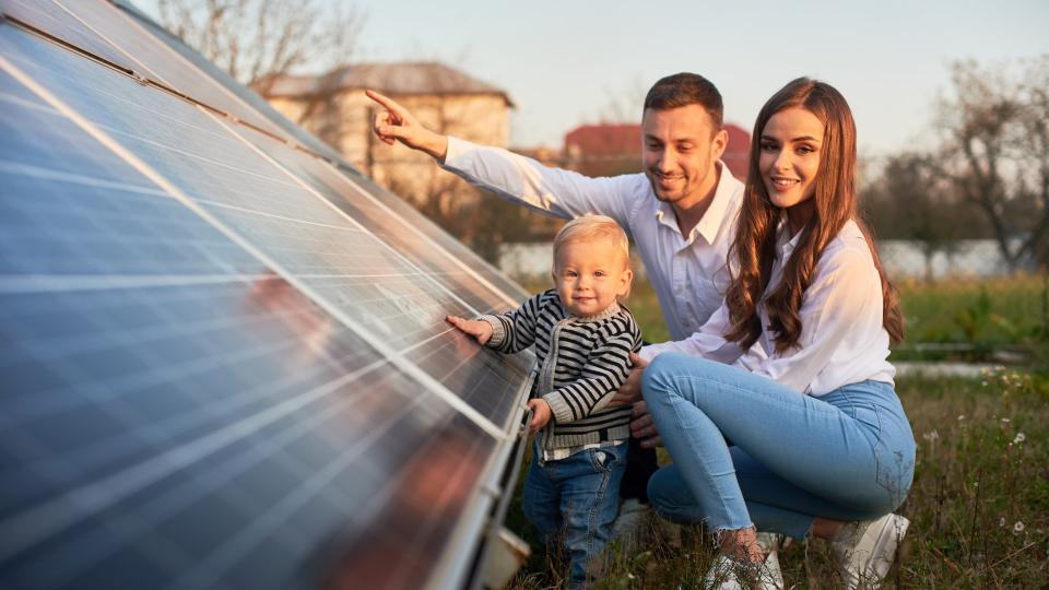 Eine dreiköpfige Famile (Vater, Mutter, Kind) untersucht eine Photovoltaikanlage.