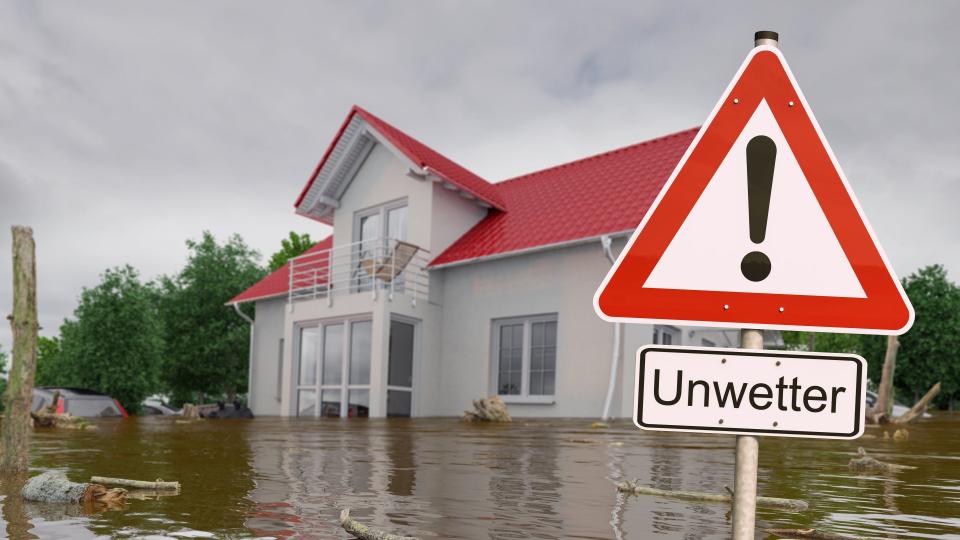Ein Haus im Hochwasser, davor ein Hinweisschild auf die Gefahr "Unwetter".
