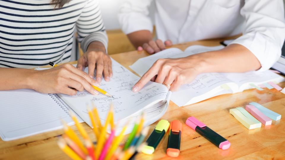 Hände von zwei Personen die gemeinsam an einem Tisch lernen.