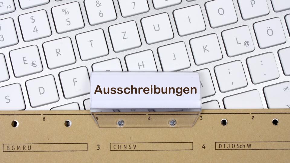 Eine Akte beschriftet mit Auschreibungen liegt auf einer Computertastatur.