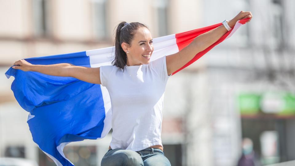 Eine junge Frau hält eine ausgebreitete Flagge Frankreichs hinter ihrem Rücken.