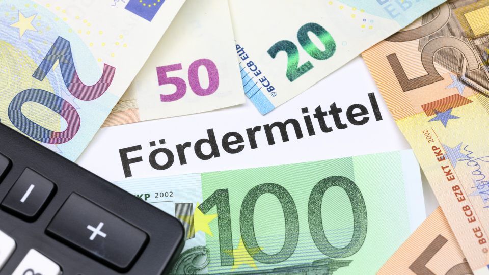 Abgebildet sind mehrere Euro-Geldscheine und ein Taschenrechner. In der Mitte des Bildes steht "Fördermittel".