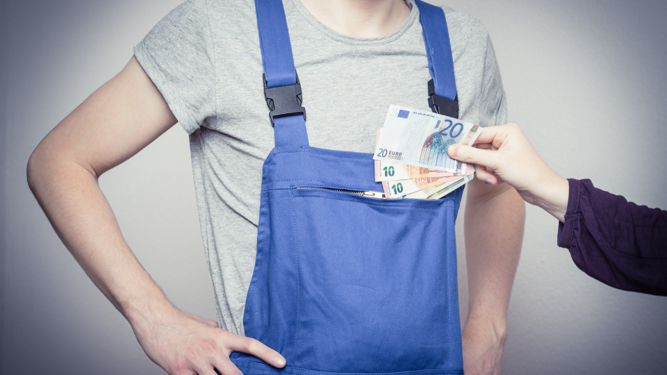 Abgebildet ist ein Handwerker in Arbeitskleidung, dem 50 Euro von einer anderen Person zugesteckt werden. 