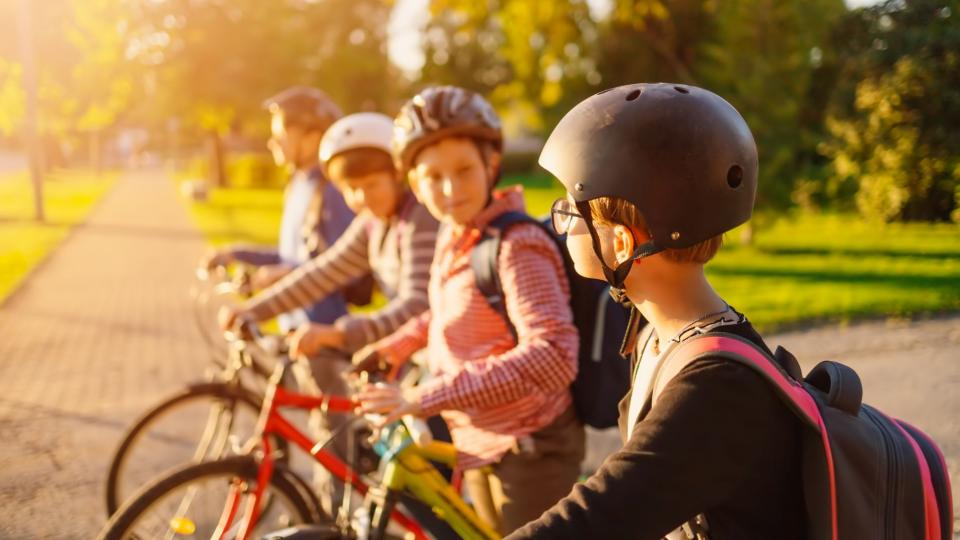 Vier Schulkinder stehen nebeneinander mit ihren Fahrrädern in einem Park. 