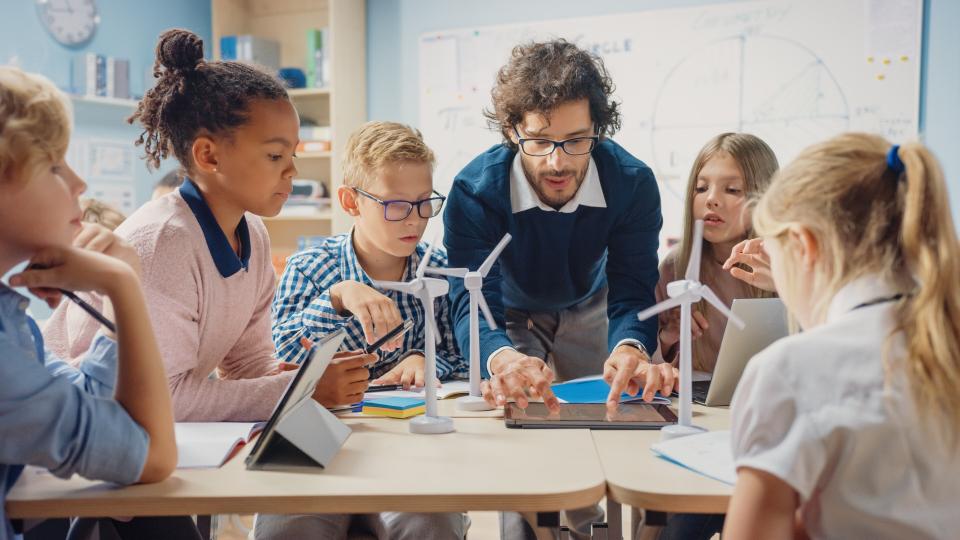 Ein Lehrer bedient ein Tablet innerhalb einer Gruppe von Schüler*innen.