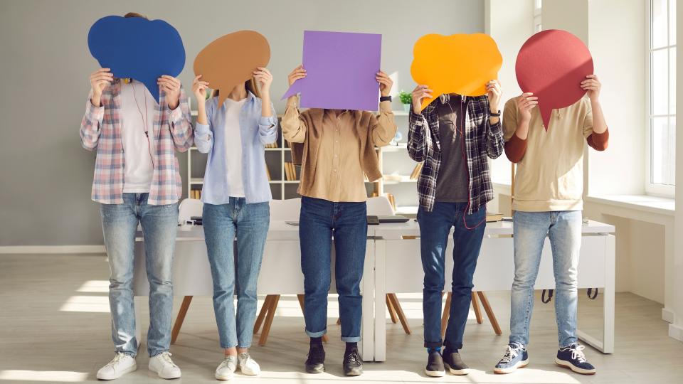 Fünf Personen in lässiger Kleidung stehen in einem hellen Raum und halten sich Sprechblasen in verschiedenen Formen vors Gesicht.