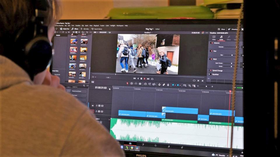 Links vorne Schulter und Schrägprofil eines Jugendlichen mit Kopfhörer, dahinter, das Bild ausfüllend ein Computer-Monitor. Darauf ein geöffnetes Videoschnittprogramm mit einem Filmbild oben und einer Tonspur unten. 