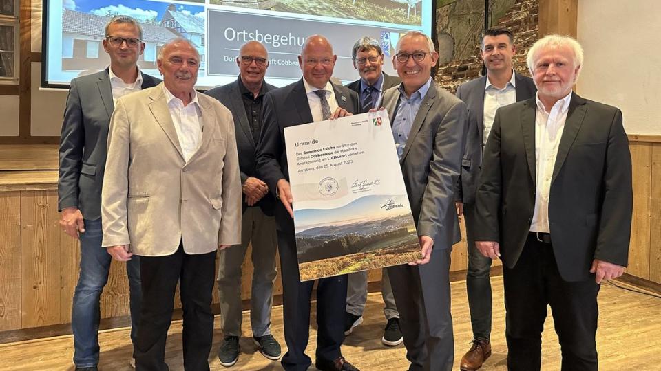 Gruppenbild. Die Ernennungsurkunde wird durch den Regierungspräsidenten und den Bürgermeister präsentiert.