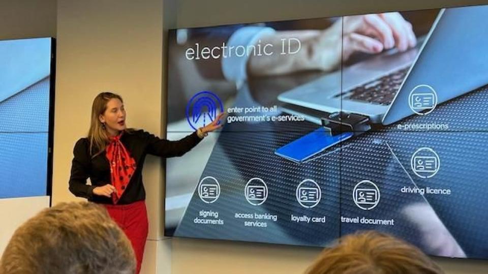 Abgebildet ist eine Frau, die eine Präsentation hält. Auf den Bildschirmen steht "electronic ID" (zu Deutsch: Online-Ausweisfunktion).