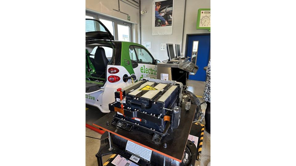 Abgebildet sind ein Elektroauto und eine ausgebaute Batterie in einer Werkstatt. 