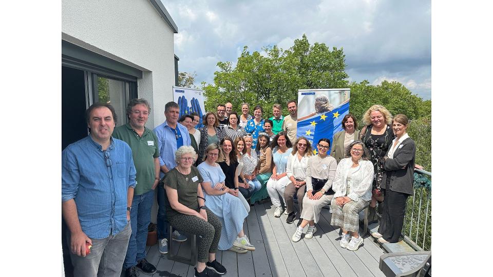 Abgebildet sind mehrere Personen, die auf einem Balkon für ein Bild posieren. 