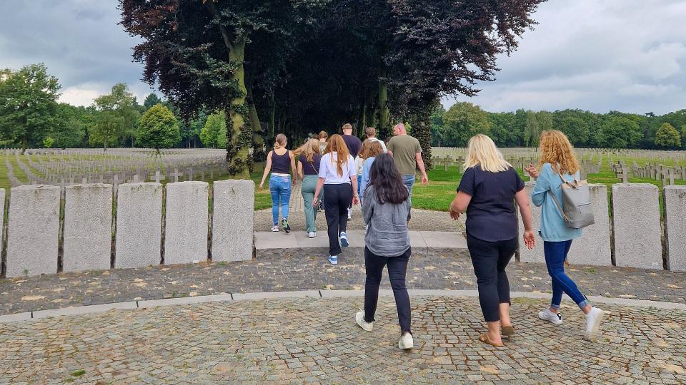 Abgebildet sind Auszubildende der Bezirksregierung Arnsberg, die auf einem Weg entlang des Friedhofs im niederländischen Ysselsteyn gehen.